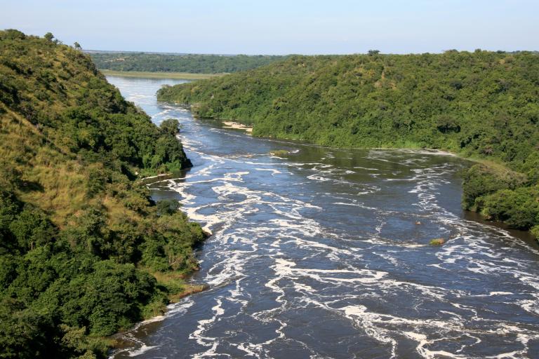 A wide river with swirling water flows between green, tree-covered hills under a clear sky.