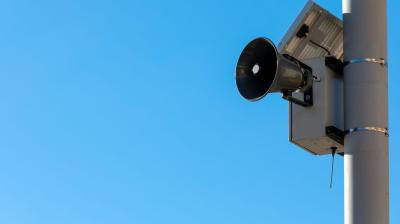 Outdoor speaker mounted on a pole against a clear blue sky.