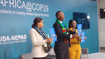 Three people stand holding booklets in front of a backdrop reading "AFRICA@COP29: Solidarity in scaling climate finance for Africa," featuring AUDA-NEPAD and COP29 branding.
