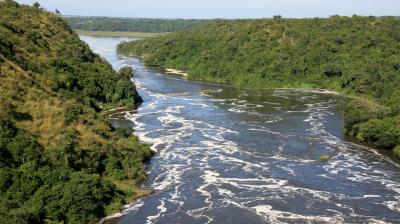 A wide river with swirling water flows between green, tree-covered hills under a clear sky.