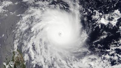 Satellite image of a large, well-defined hurricane with a visible eye over the ocean near a landmass, surrounded by dense clouds.