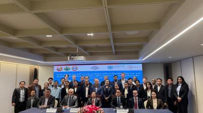 A group of people in business attire pose for a photo at a conference table, with a banner and flower arrangement in the background.