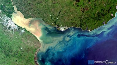 Satellite image shows a river delta emptying into the ocean near Montevideo, Uruguay, with sediment plumes visible in the water and urban and rural areas on land.