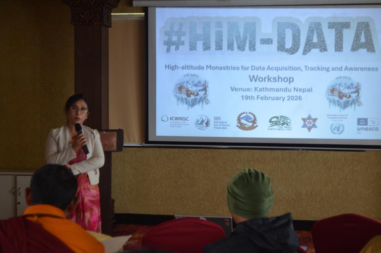 A woman speaks at a podium beside a screen displaying details for the HiM-DATA workshop in Kathmandu, Nepal, scheduled for 19th February 2026.